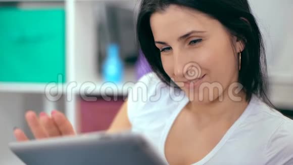 漂亮的女人在家里坐在沙发上用数码平板电脑视频的预览图
