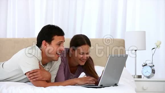 可爱的一对夫妇用笔记本电脑躺在床上视频的预览图
