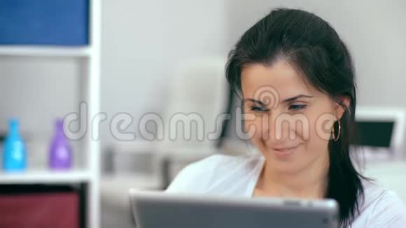 漂亮的女人在家里坐在沙发上用数码平板电脑视频的预览图