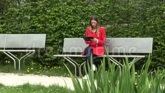 穿着红色连衣裙的女孩在公园的街上拿着一块平板电脑视频的预览图