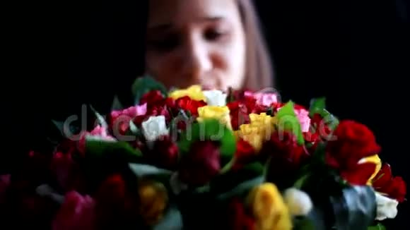 美丽的微笑着的女人怀里抱着一大束鲜花闻着一朵芬芳的五颜六色的玫瑰在黑色上视频的预览图