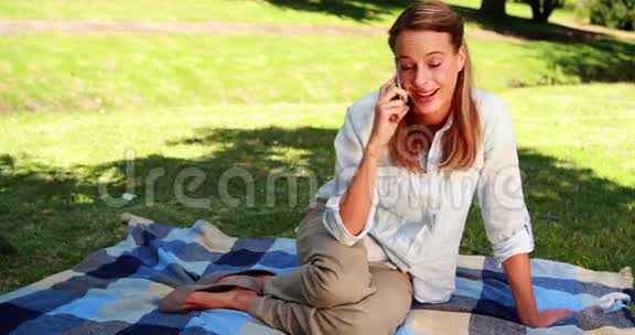 坐在公园的毯子上打电话聊天的金发美女视频的预览图