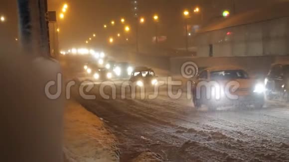 汽车沿着积雪覆盖的傍晚道路行驶在大雪中灯光亮起视频的预览图