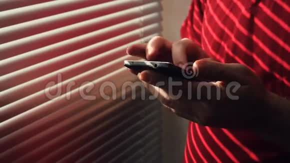 一个带智能手机的人站在窗户边带百叶窗视频的预览图