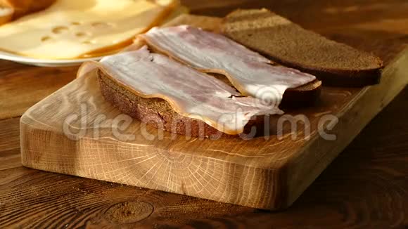 夹着培根和奶酪的三明治黑面包配培根和香料盘子上有洞的奶酪切成薄片的猪肉视频的预览图
