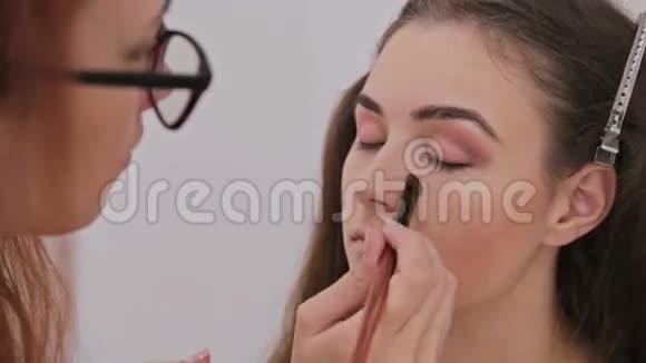 化妆师将化妆涂在美丽的年轻性感模特的脸上视频的预览图