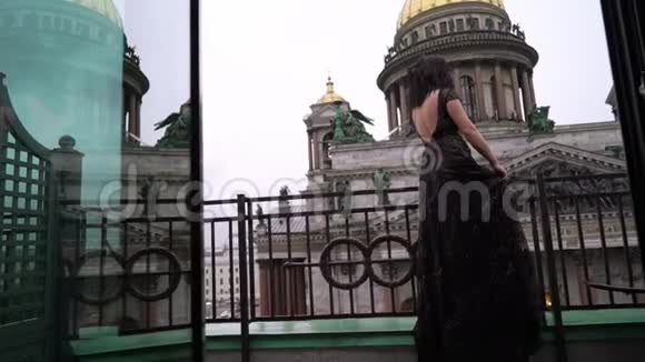 年轻的黑发女人穿着黑色豪华礼服住在城市的阳台上视频的预览图