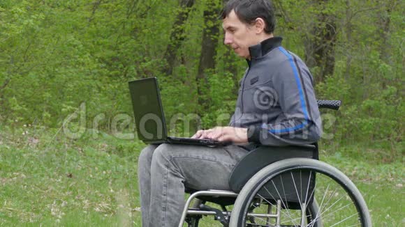 残疾人视频聊天轮椅与笔记本电脑在轮椅上工作的自然绿色背景视频的预览图