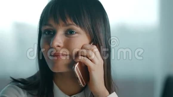一位年轻女子坐在电脑后面的办公室里的办公桌前打着电话笑视频的预览图