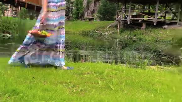 穿着衣服的孕妇带着篮子的水果走在河边视频的预览图