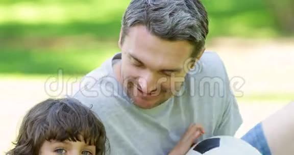 父亲和小儿子坐在公园里踢足球视频的预览图