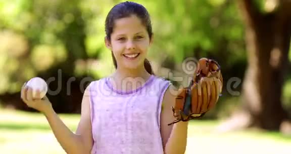 运动的小女孩在公园里玩棒球对着镜头微笑视频的预览图