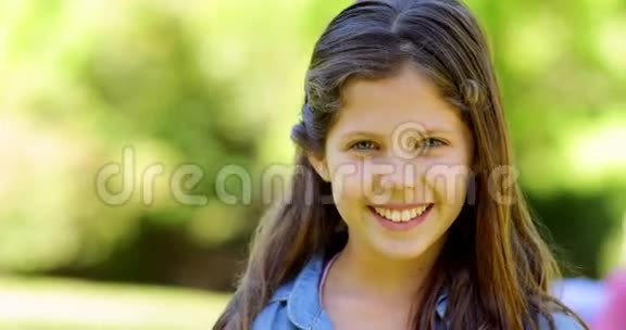 小女孩在镜头前微笑父母在公园长凳后面视频的预览图