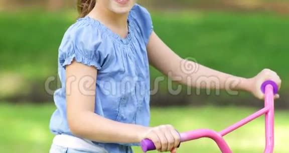 小女孩在粉色自行车上微笑着对着镜头挥手视频的预览图