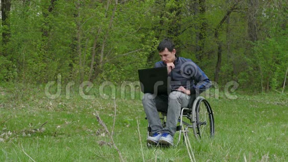 残疾人认为轮椅上有一台笔记本电脑坐在轮椅上在绿色的背景下工作已经厌倦了休息问题视频的预览图