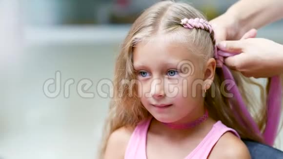 美丽的金发女孩七岁梳着两条辫子在美容院做一个粉红色头发的发型视频的预览图