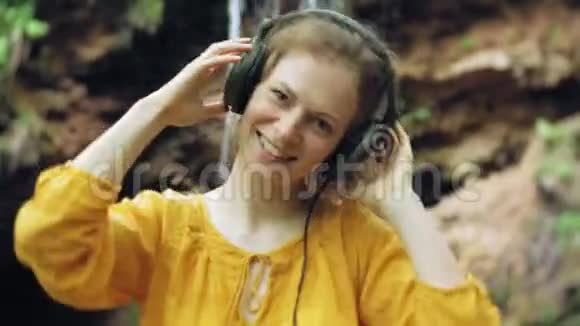 年轻时尚的美女靠近瀑布听音乐的大监控耳机视频的预览图
