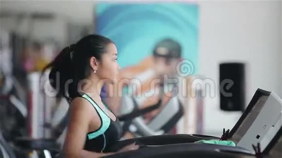 漂亮的亚洲女孩在健身房的跑步机上跑步右侧脸照片视频的预览图