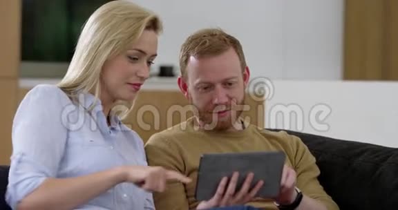 客厅里漂亮的年轻情侣在迷你平板电脑上上网视频的预览图