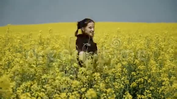 穿着黑色衣服的年轻女子穿着黄色的衣服穿过黄色的田野抚摸着鲜花高清视频的预览图