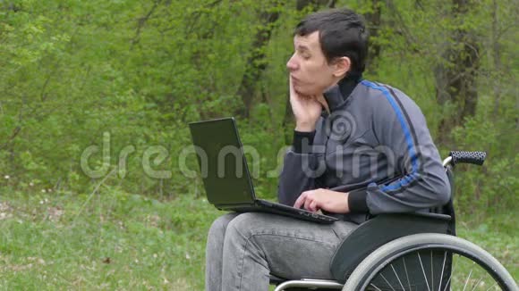 残疾人认为在自然绿色背景下轮椅和笔记本电脑在工作时已经厌倦了休息问题视频的预览图