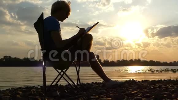 年轻人坐在河岸的折叠椅上写在日落的斯隆莫视频的预览图