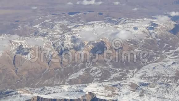 令人惊叹的山脉美景微微覆盖着雪从云中掠过从飞机窗口眺望视频的预览图