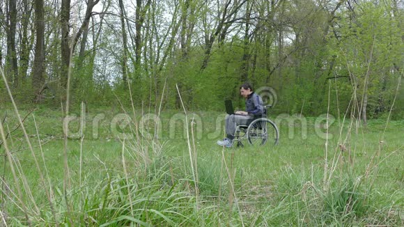 残疾人认为轮椅上的笔记本电脑在自然绿色背景下工作已经很累了视频的预览图