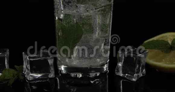 用绿色薄荷叶和黑色背景的冰块倒入杯中视频的预览图