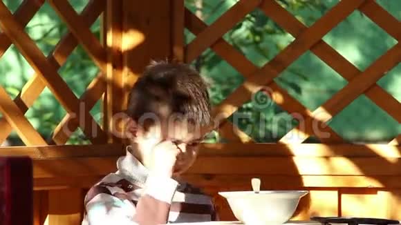 男孩在户外的露台上吃饭困倦的男孩害羞的相机视频的预览图