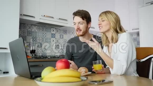 一对年轻夫妇在厨房吃早餐时用手提电脑说话视频的预览图