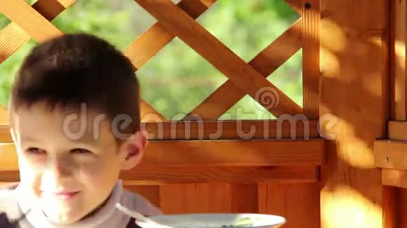 男孩在户外的露台上吃饭困倦的男孩害羞的相机视频的预览图