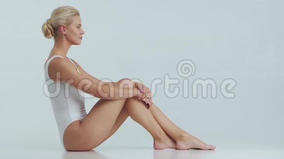 年轻美丽健康和自然的金发女人穿白色泳衣涂上护肤霜按摩护肤脂肪视频的预览图