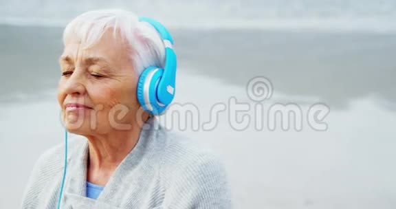 在海滩上听耳机音乐的高级女性视频的预览图