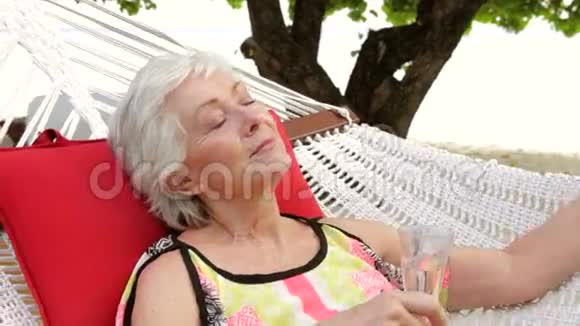 老年妇女在沙滩吊床上享受香槟放松视频的预览图