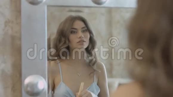 美丽的女孩站在镜子前用刷子把粉末涂在脸上视频的预览图