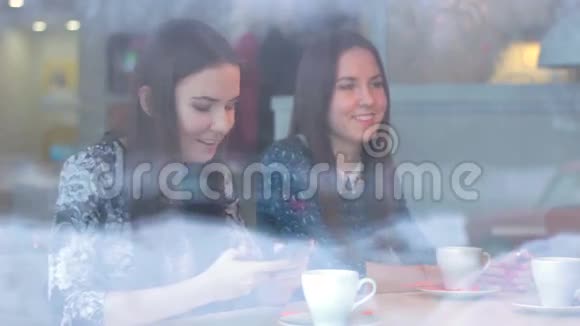 漂亮的女孩在咖啡馆里展示智能手机女朋友视频的预览图