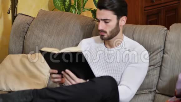 英俊的年轻人在家看书坐在沙发上视频的预览图