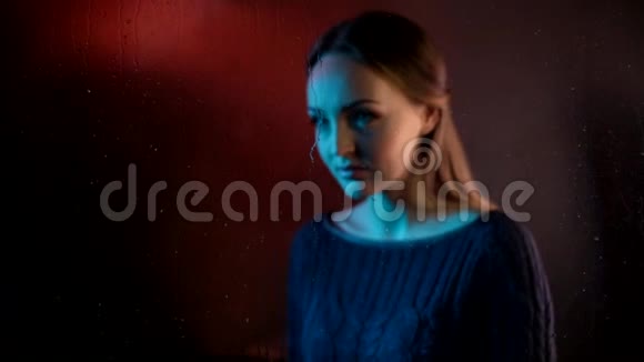 忧伤梦幻的年轻女子靠近蒸汽玻璃窗触摸着令人心驰神往的手掌手指在夜色中泛着蓝色的霓虹视频的预览图