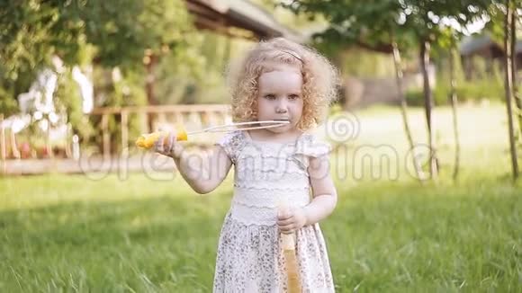 一个小女孩吹着肥皂泡特写肖像美丽的卷发婴儿视频的预览图