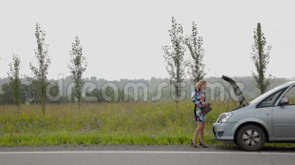 一个美丽的女孩在乡间小路上的破车旁打电话视频的预览图