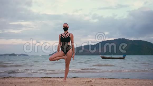 穿着黑色泳衣和医用防烟面具在海滨练习瑜伽的高加索女人视频的预览图