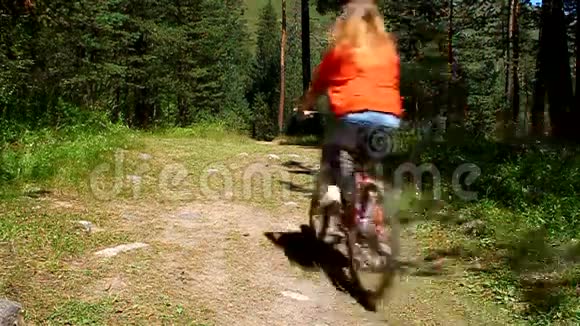 女孩骑自行车在森林里的土路上视频的预览图