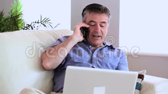 快乐的男人拿着笔记本电脑在沙发上打电话视频的预览图