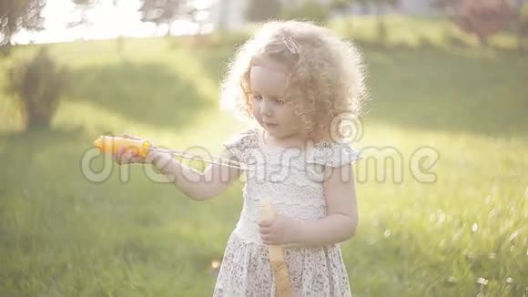 一个小女孩吹着肥皂泡特写肖像美丽的卷发婴儿视频的预览图