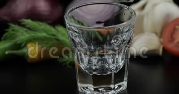 把酒精伏特加从一个瓶子里倒入酒杯蔬菜背景视频的预览图