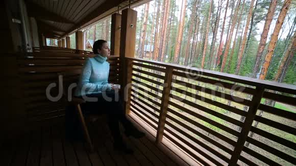 穿着蓝色毛衣的女孩坐在木椅上喝茶视频的预览图
