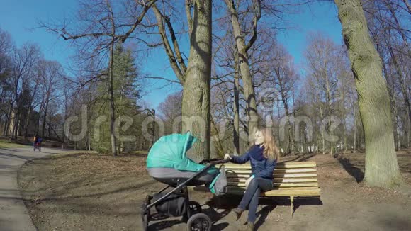 年轻的母亲带着孩子坐在马车上坐在公园的长凳上4K视频的预览图