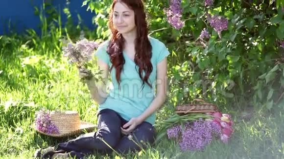 美丽的女人带着一束紫丁香坐在草地上的春天公园里视频的预览图