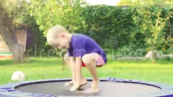 快乐的金发男孩在夏日花园的蹦床上跳视频的预览图